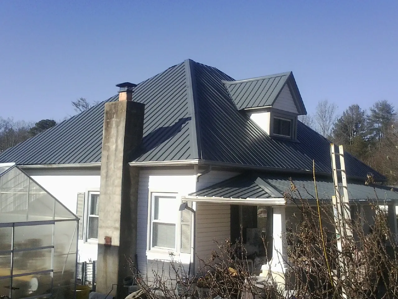 Dark blue standing seam metal roof on a white farmhouse with dormer — Slate & Tile Roof Repair by Roofing Brothers in Bessemer