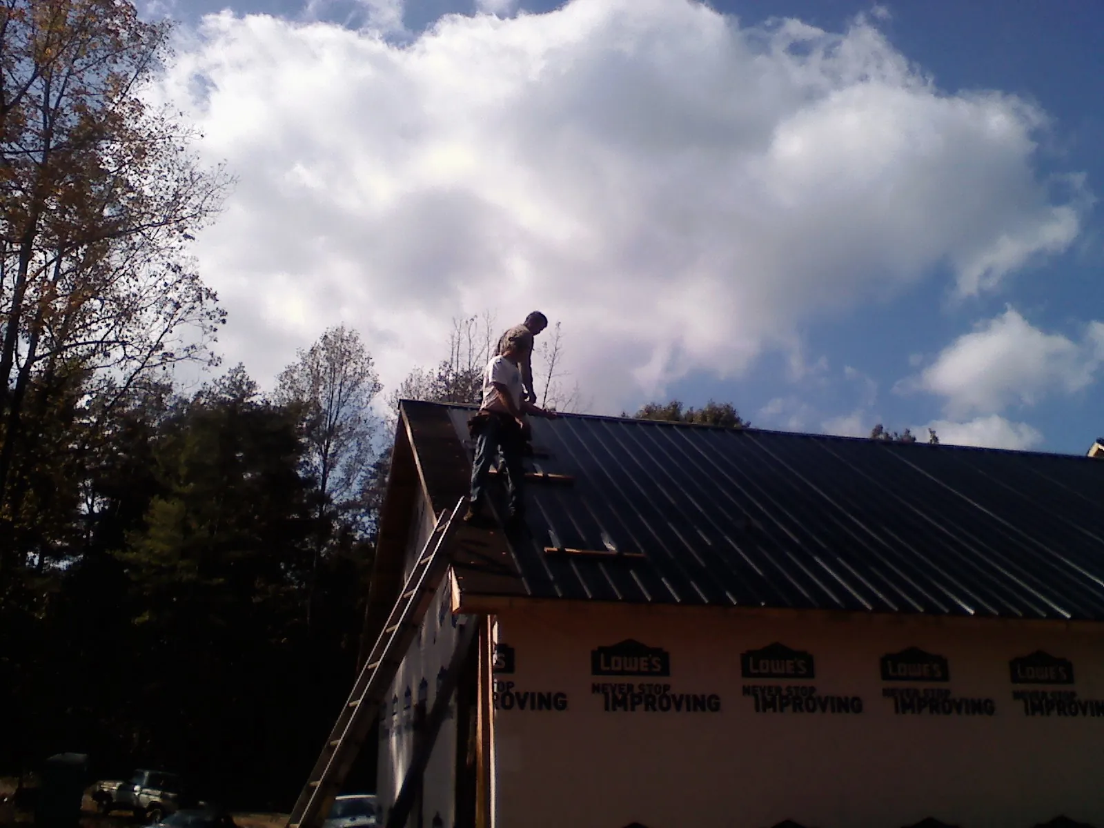 Roofer fastening dark metal panels high against a cloudy sky, from a Roof Inspection job in Bessemer
