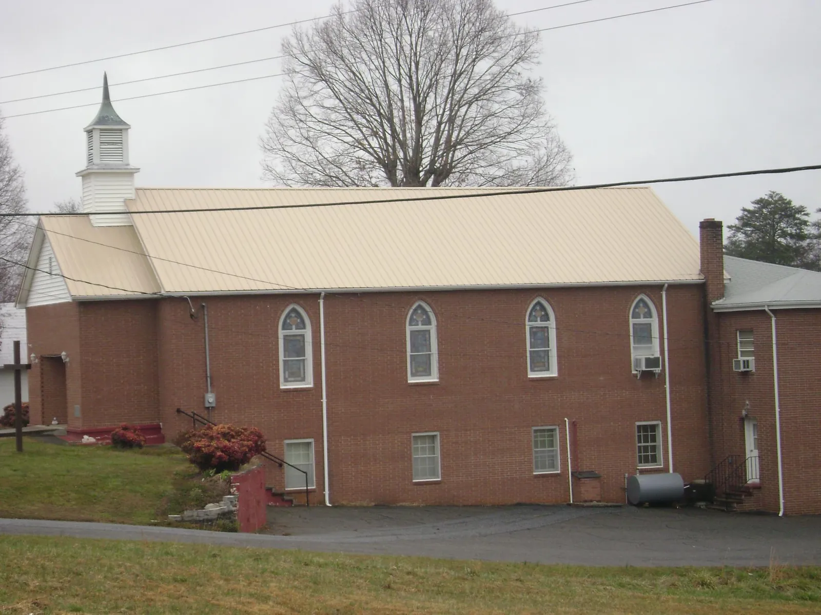 New tan metal roof on a brick church with a white steeple in Bessemer