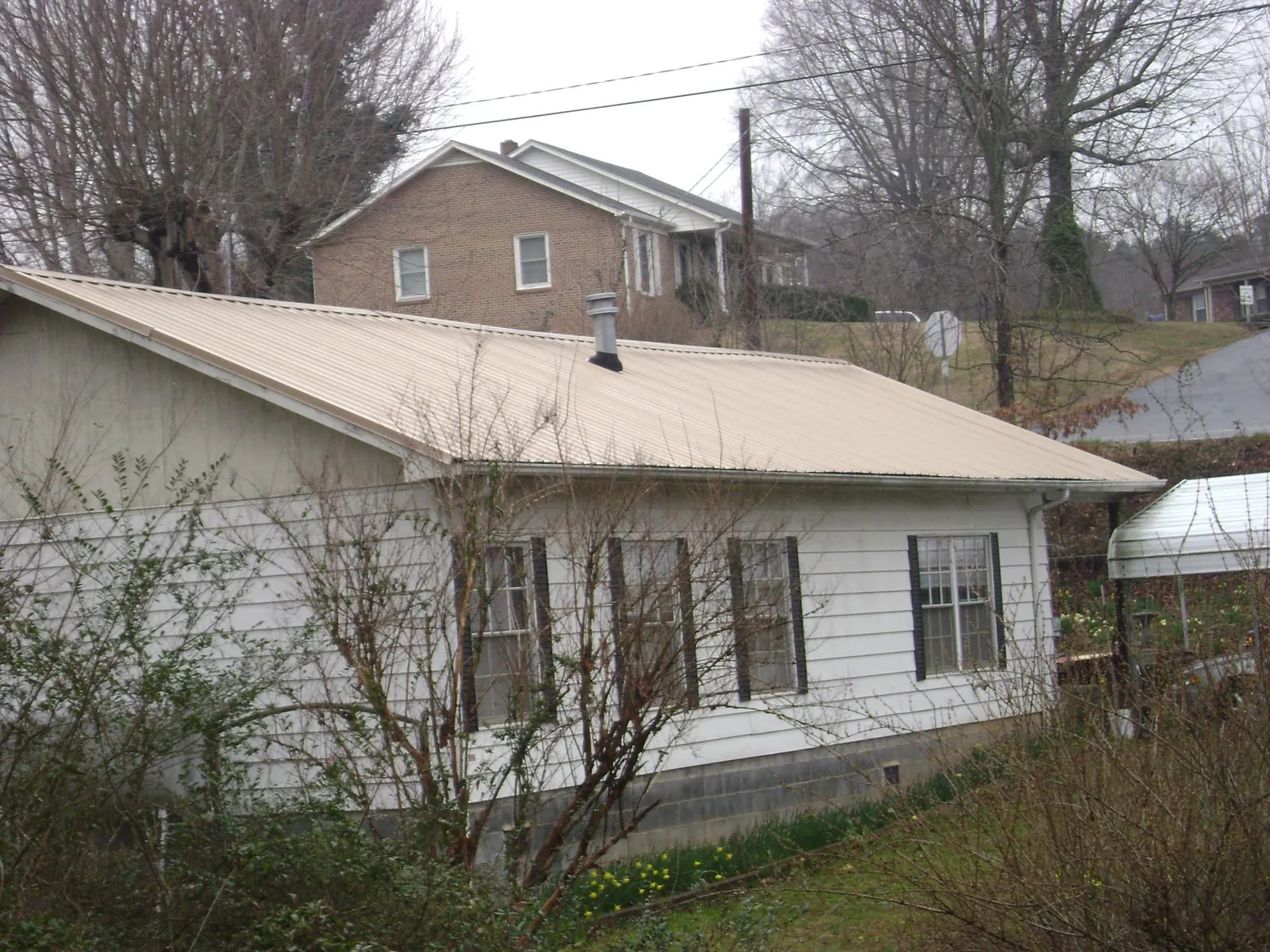 Tan metal roof on a white sided house set into a hillside — Commercial Roofing by Roofing Brothers in Bessemer