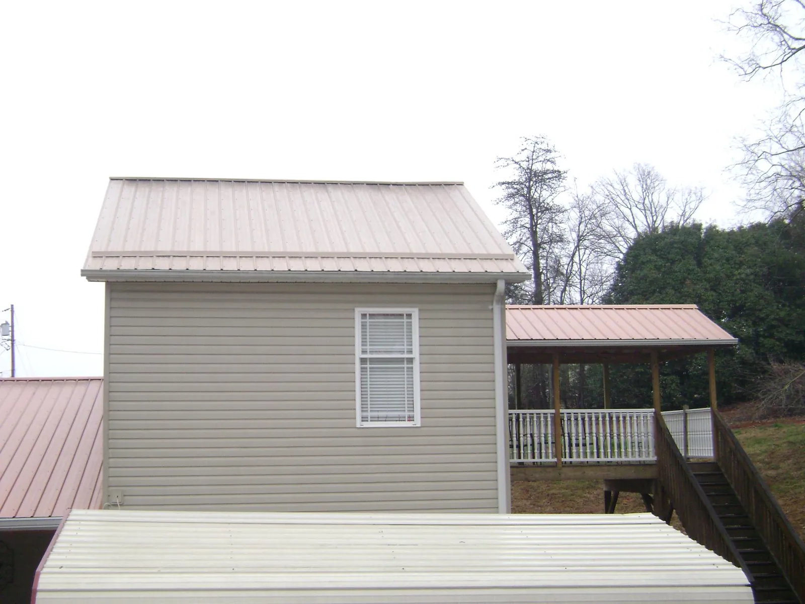 Tan metal roofs on a two story addition and attached porch, from a Roof Replacement job in Bessemer
